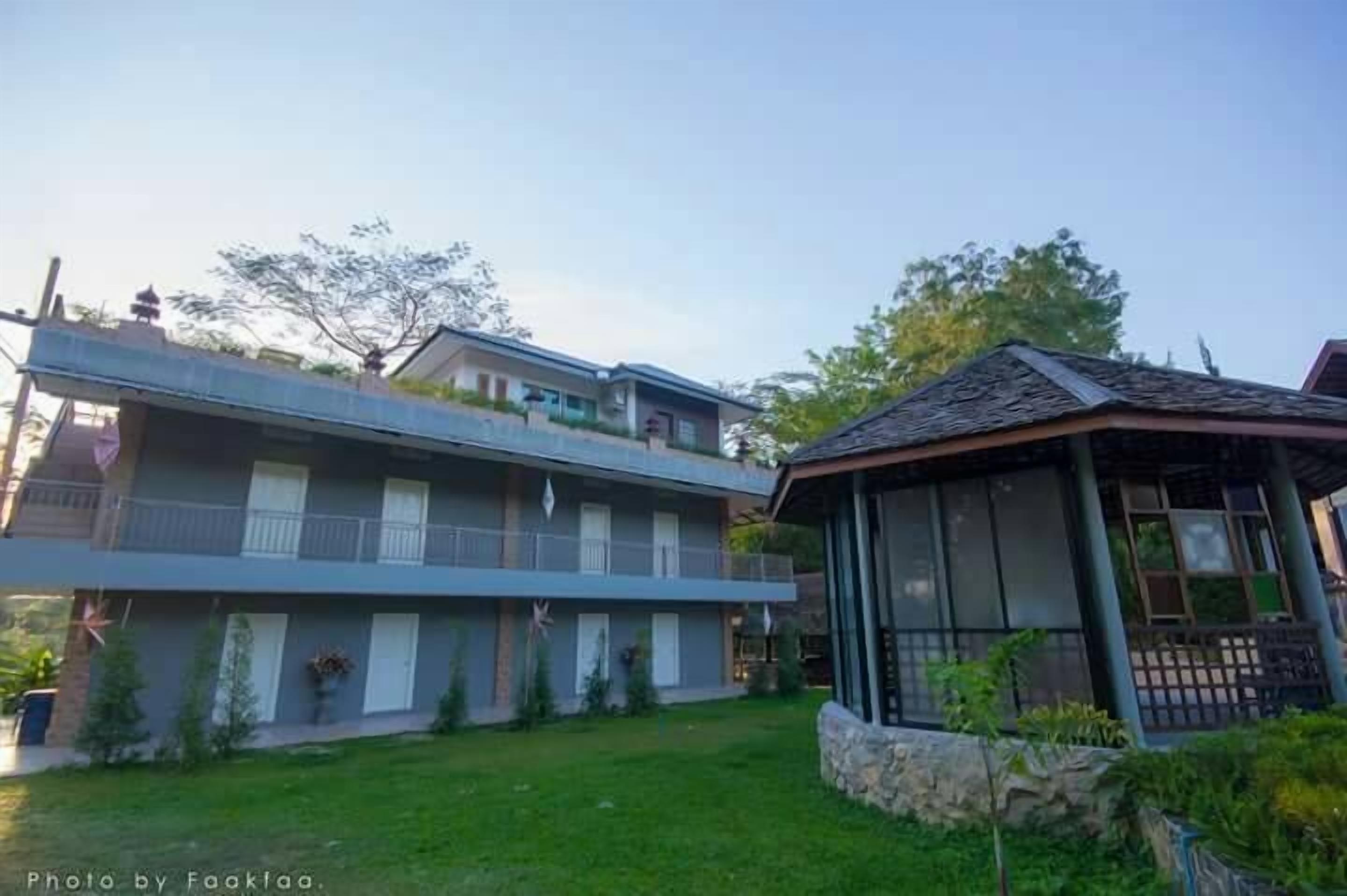 Un edificio de dos plantas con un balcón en el piso superior, un espacio al aire libre cubierto y un césped bien cuidado.