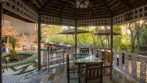 A covered outdoor dining area with tables and chairs, surrounded by a wooden fence and potted plants. - Season Namkorn Resort (Chiang Rai)