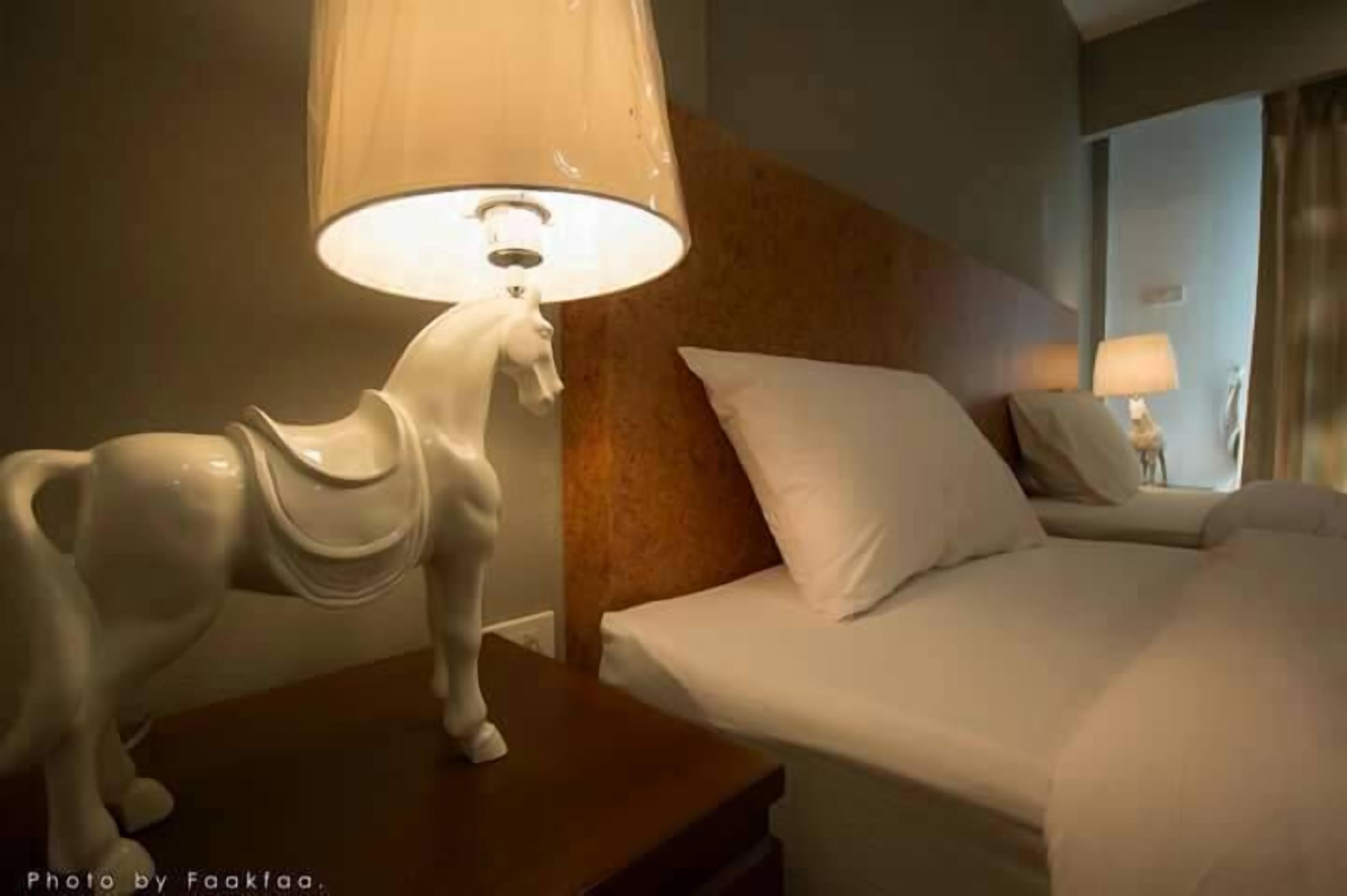 A hotel room with a bed, a nightstand, a lamp with a horse-shaped shade, and a mirror on the wall.