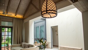 A spacious living room with a high ceiling, a large window with blinds, a sofa, a coffee table, and a hanging light fixture. - Flora Creek Resort & Garden Chiang Mai (Chiang Mai)