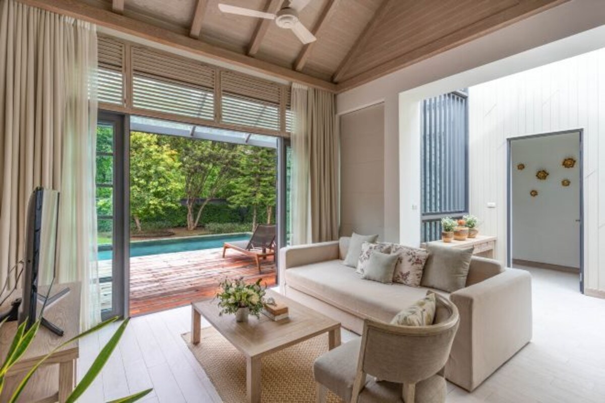 Amplia sala de estar con sofá, mesa de centro, sillas, televisor y vista a una piscina.
