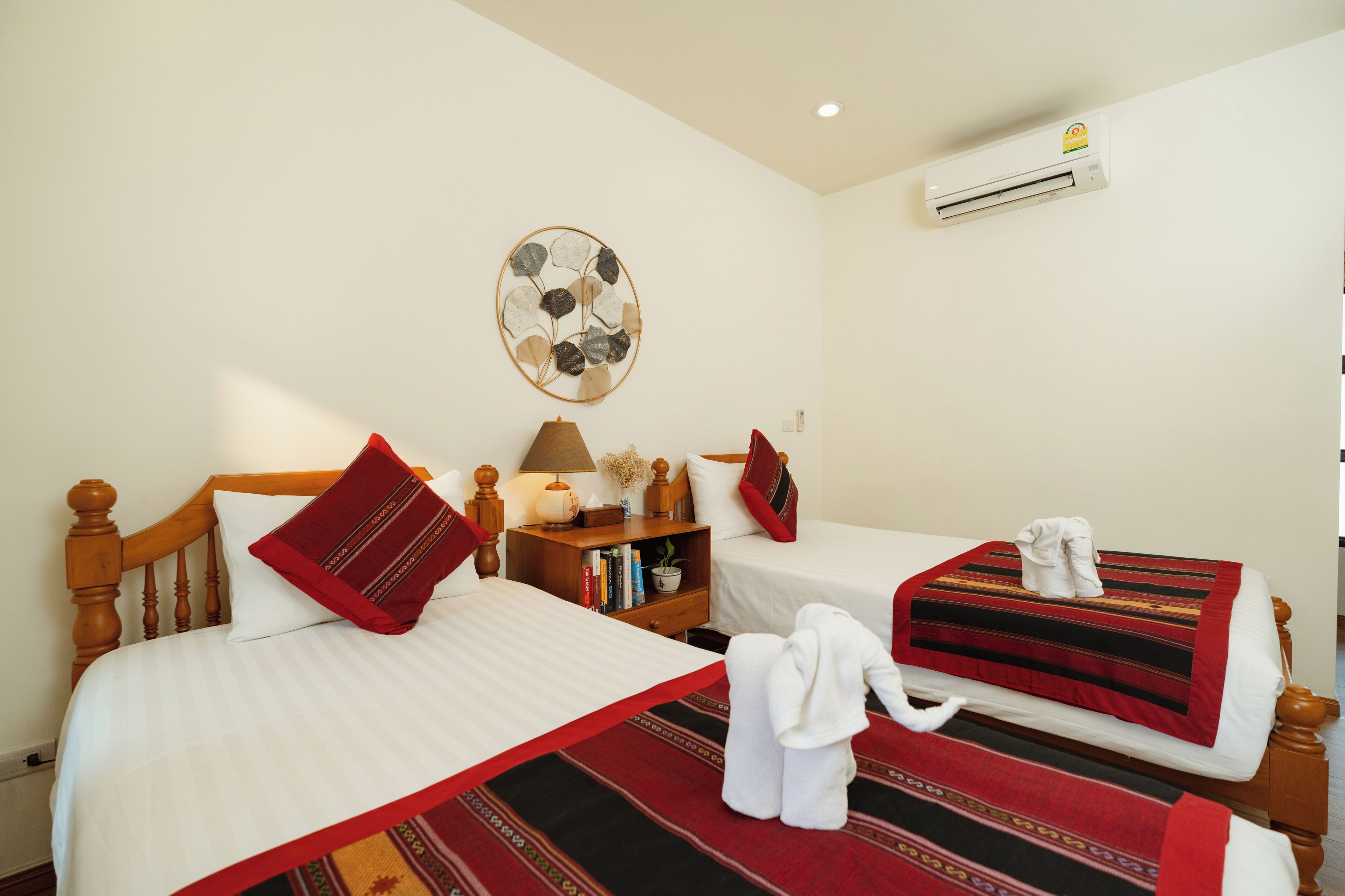 A hotel room with two beds, a bedside table with a lamp, a wall-mounted air conditioner, and a decorative wall piece.