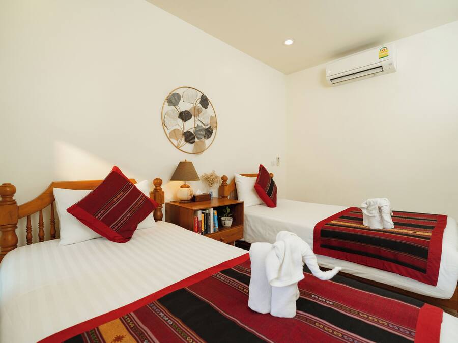 A hotel room with two beds, a bedside table with a lamp, a wall-mounted air conditioner, and a decorative wall piece.