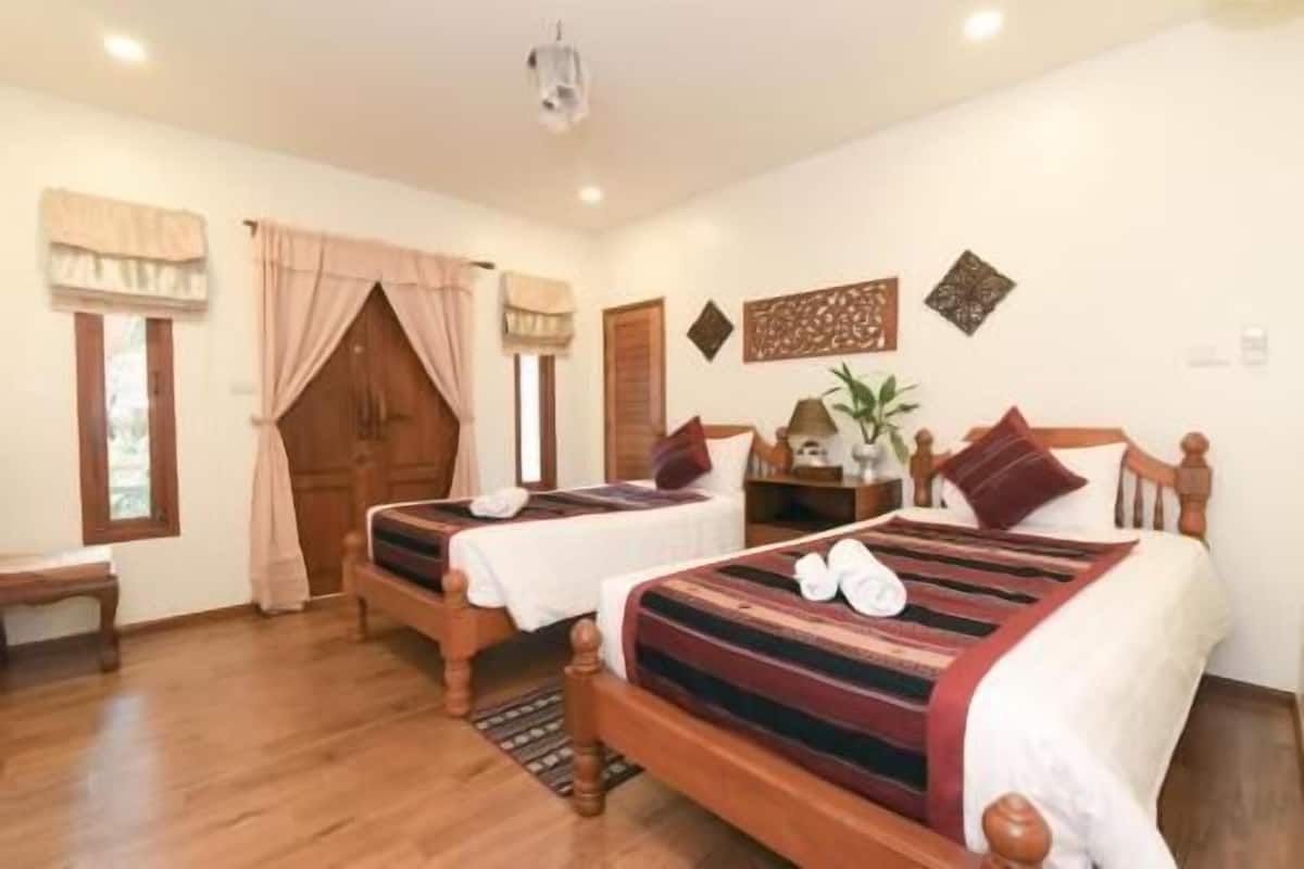 A hotel room with two wooden beds, a wooden bench, a small table, and a ceiling light.