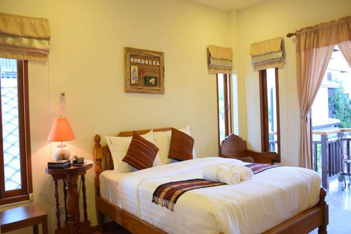 A bedroom with a bed, a bedside table with a lamp, a window with curtains, and a sign on the wall.