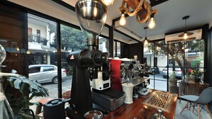 Interior de uma cafeteria com uma máquina de café, uma mesa de madeira e vista para a rua.