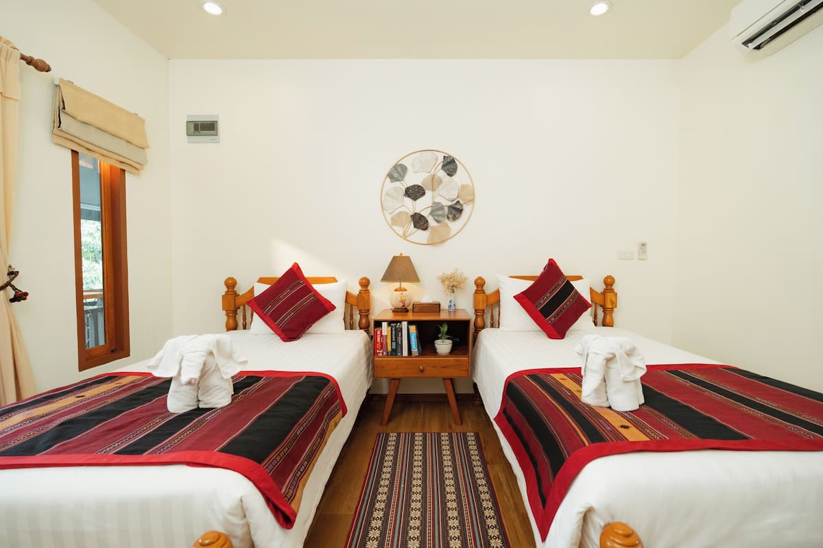 A hotel room with two beds, each with a red and black striped bedspread, a wooden nightstand with books and a lamp, and a wall-mounted decorative plate.