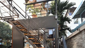 Escadaria moderna ao ar livre, com degraus de madeira e corrimãos de metal, que leva a um espaço coberto com plantas em vasos e área de estar.