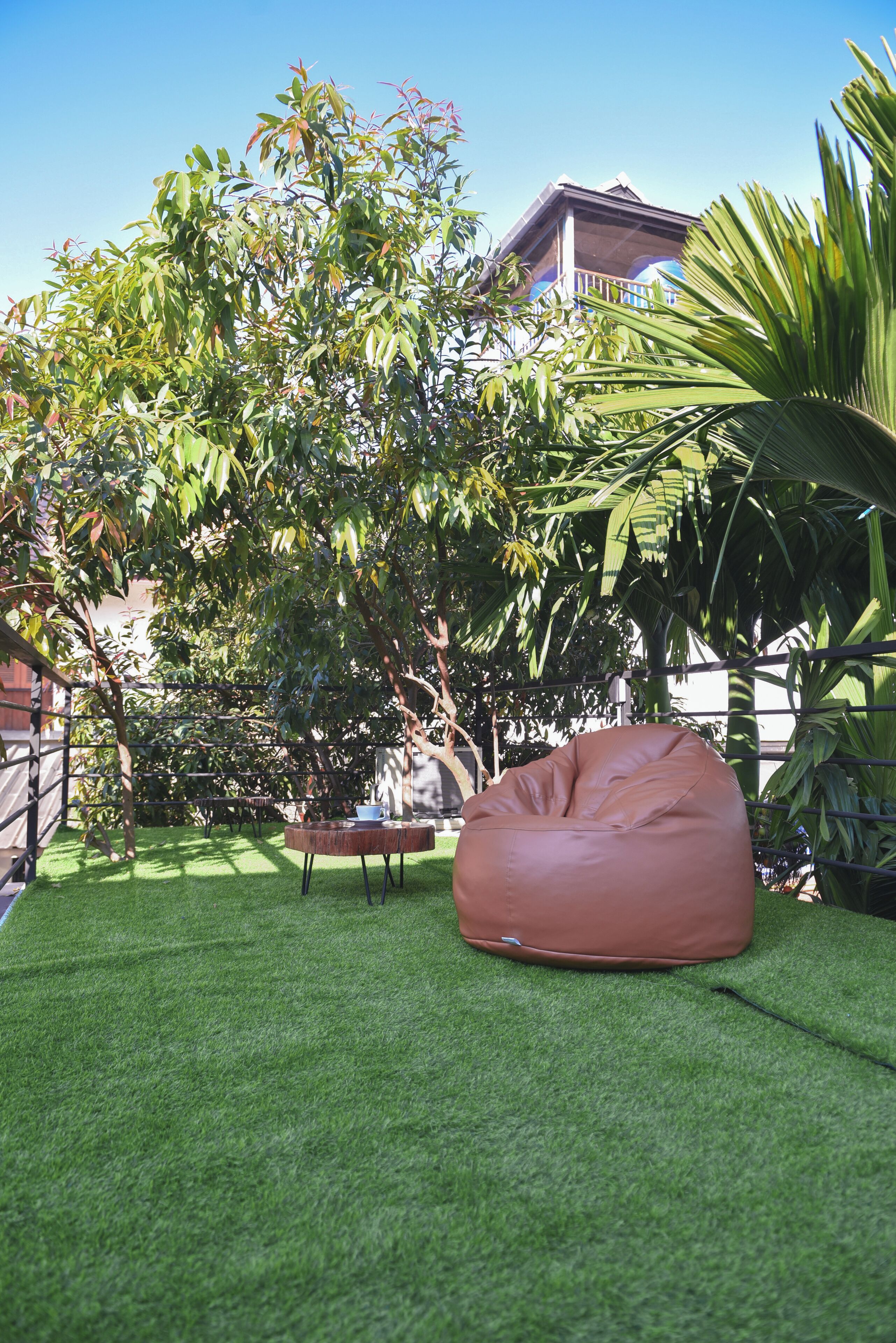 A garden with a green lawn, a brown bean bag, and a table with a cup and saucer.