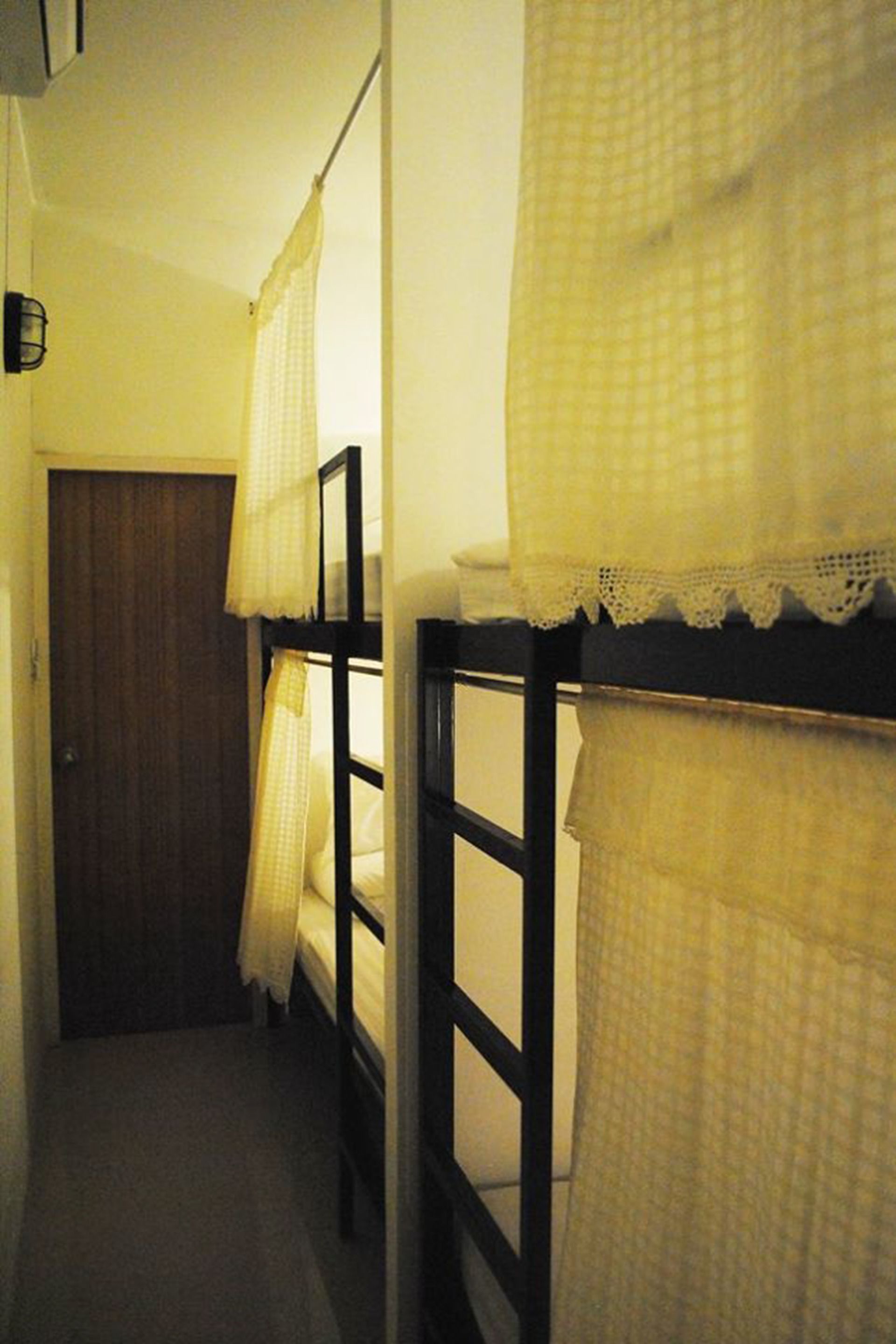 Un couloir étroit avec des lits superposés, une porte en bois et une petite fenêtre avec un rideau.