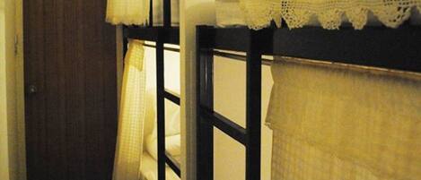 Un couloir étroit avec des lits superposés, une porte en bois et une petite fenêtre avec un rideau.