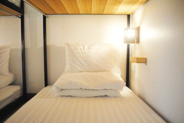 A single bed with white bedding in a room with a wooden ceiling and a wall-mounted light fixture. - Rimnim Hostel (Chiang Mai)