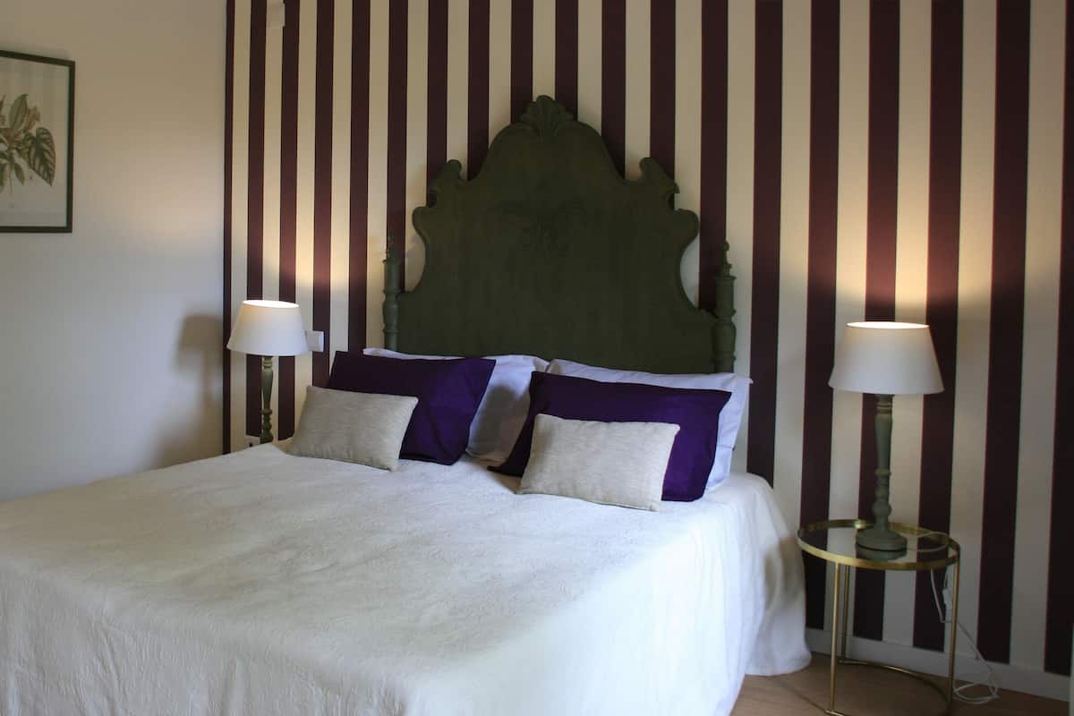 A bed with a headboard, two bedside lamps, and a wall with vertical stripes.