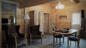 A wooden interior with a dining table, two chairs, a floor lamp, and a chandelier.