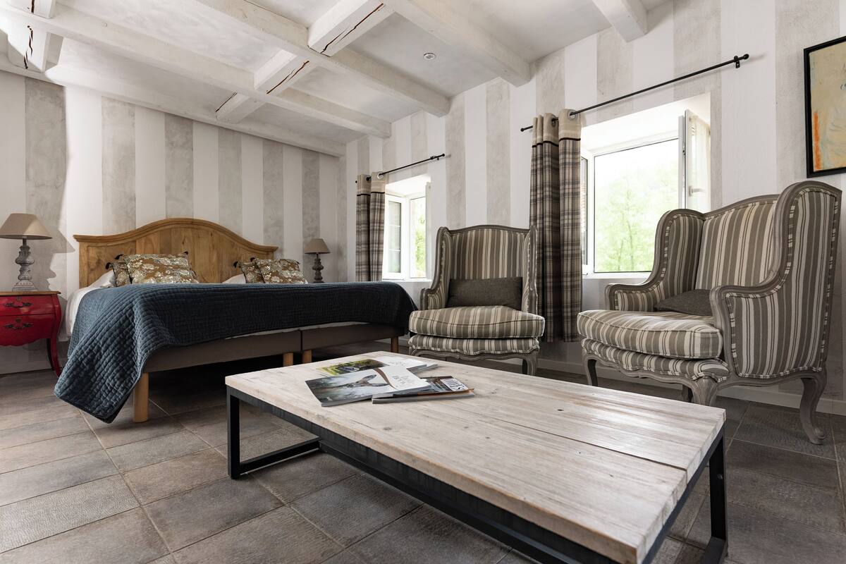 Une chambre à coucher comprenant un lit, deux fauteuils, une table basse en bois et une table de chevet avec une lampe.