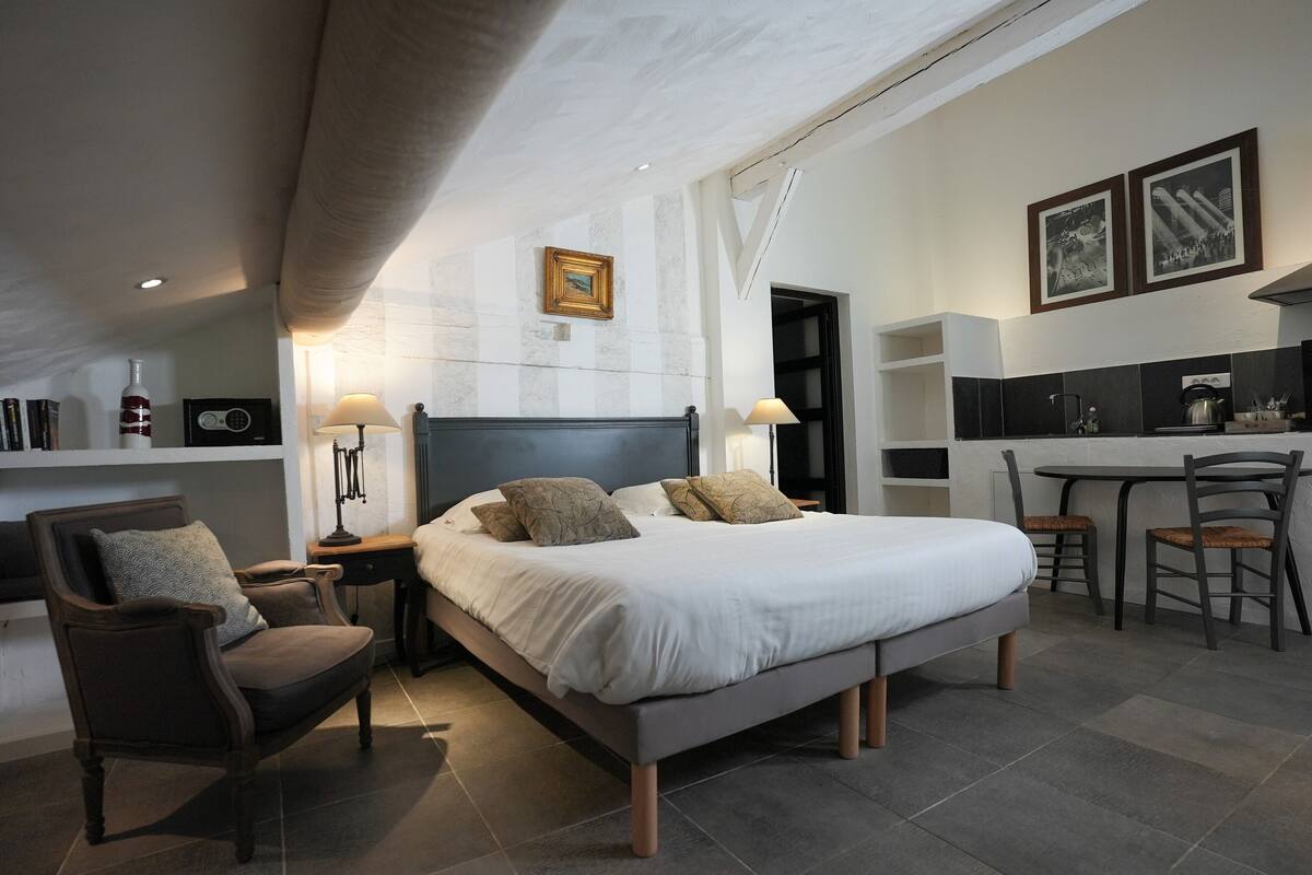 Une chambre d’hôtel moderne avec un grand lit, un bureau et une chaise. Elle comprend également un petit coin cuisine équipé d’une cuisinière et d’un évier.