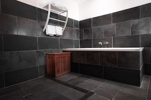 A modern bathroom with dark tiled walls, a wooden bench, and a white bathtub. - Auberge de La Poulcière (Gerardmer)