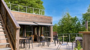 A wooden deck with outdoor seating, a staircase, and a glass-enclosed area.