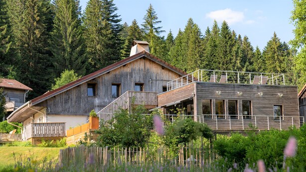 A rustic wooden house with a balcony and a modern extension.