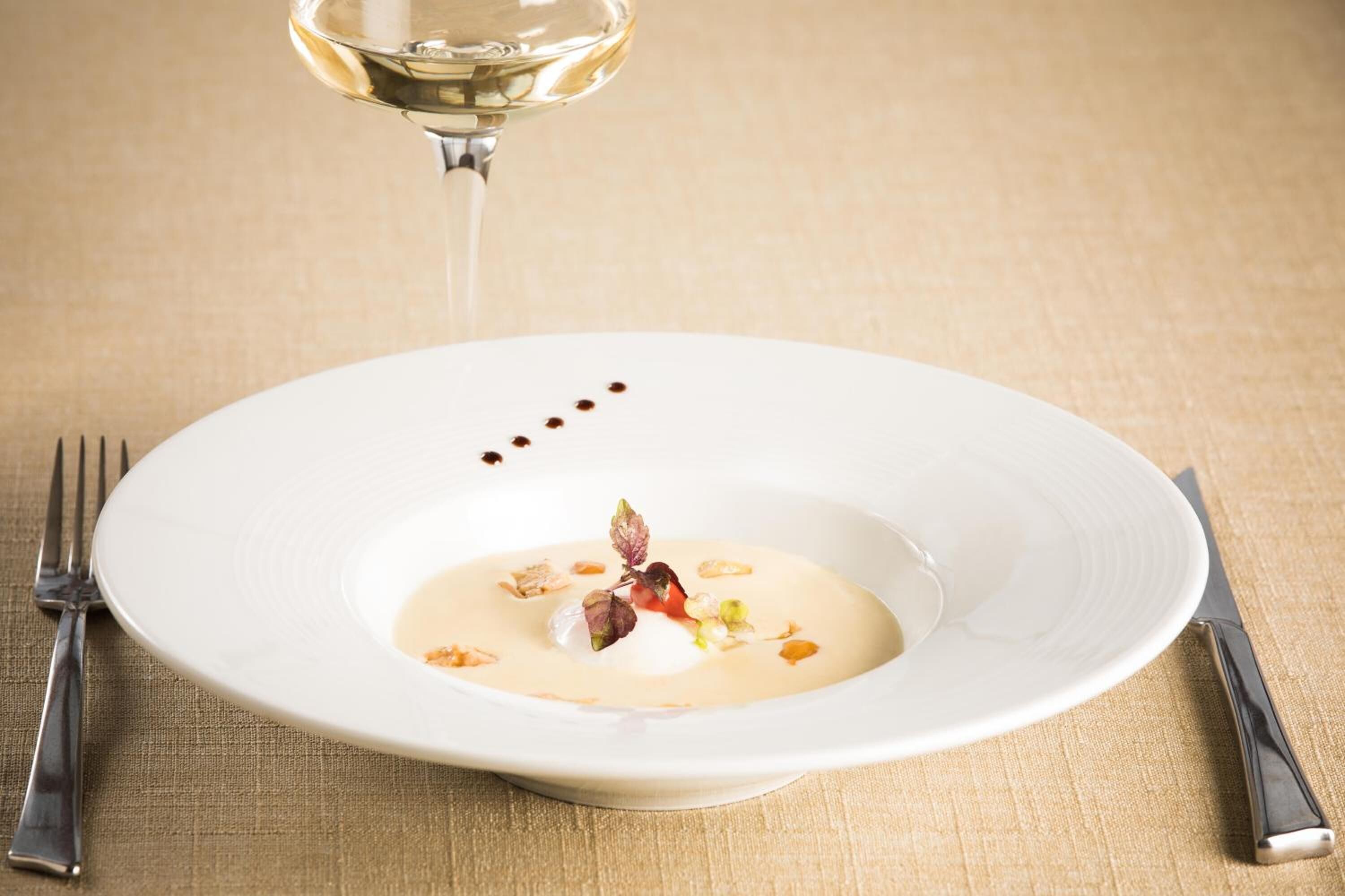 Une assiette blanche contenant un dessert crémeux, décoré de noix et d’une fleur, posée sur une nappe à motifs.