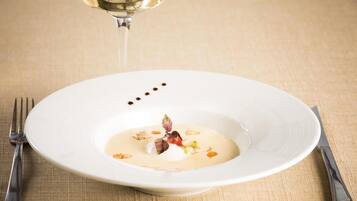 Une assiette blanche contenant un dessert crémeux, décoré de noix et d’une fleur, posée sur une nappe à motifs.