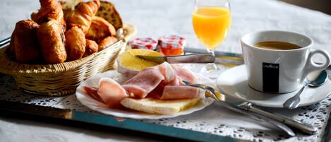 A breakfast tray with croissants, ham, cheese, toast, and a glass of orange juice.