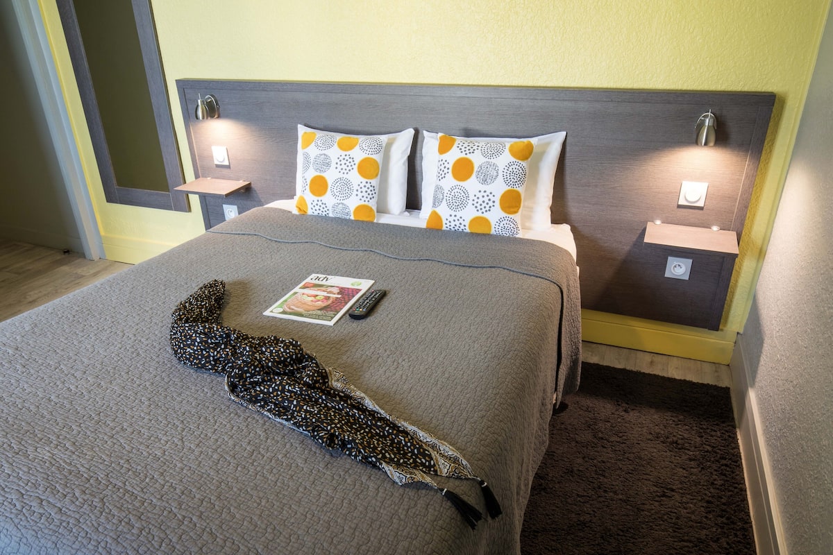 Een net opgemaakt bed met een tijdschrift, kussens met stippen en bedlampjes.