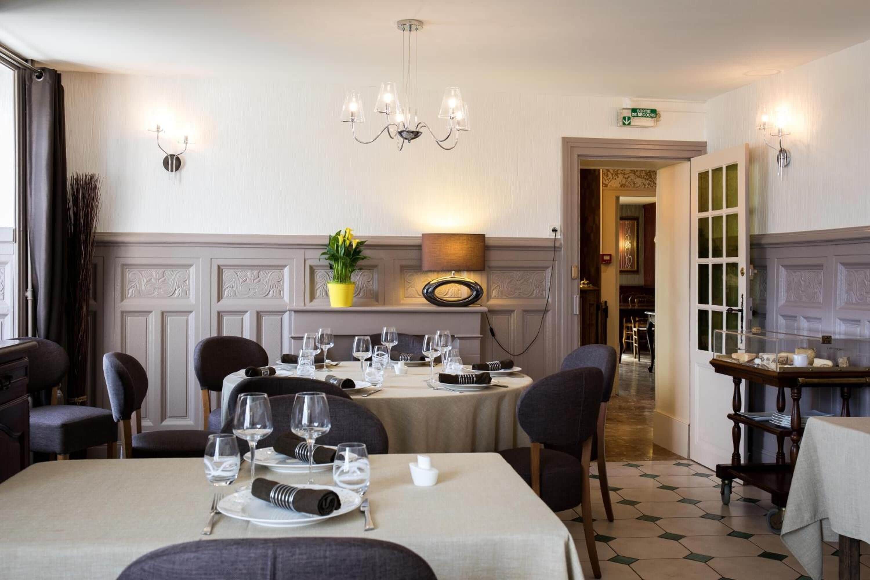 A dining area with tables set for a meal, a chandelier, and a plant on a shelf.