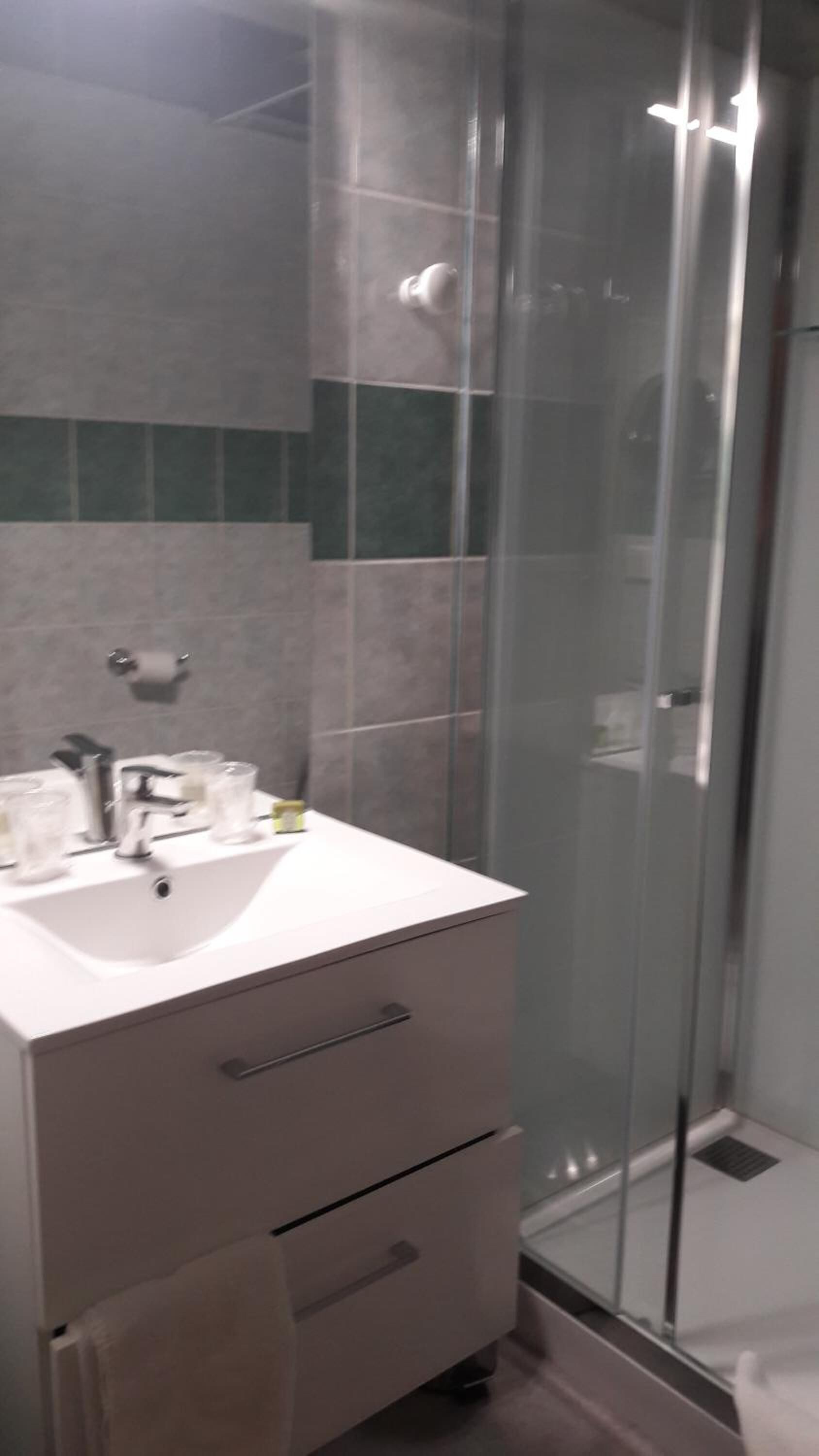 A modern bathroom with a glass shower enclosure, a white sink, and a vanity with drawers.