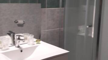 A modern bathroom with a glass shower enclosure, a white sink, and a vanity with drawers.