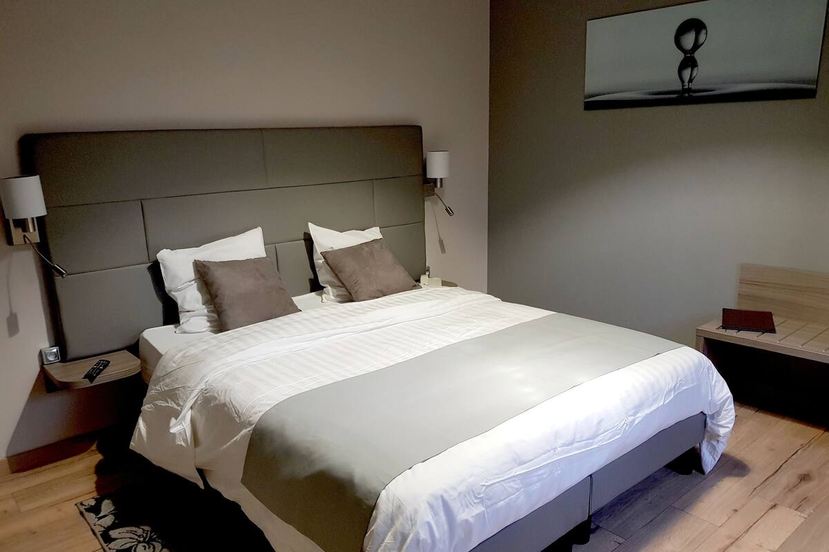 Un lit bien fait, avec une tête de lit, des tables de chevet dotées de lampes et une œuvre d’art accrochée au mur.