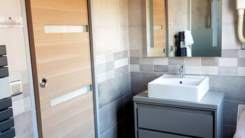 A modern bathroom with a wooden door, a sink, a mirror, and a towel rack.