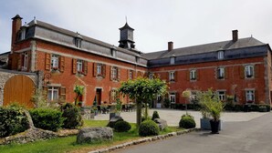 A historic building with red brick walls, multiple windows, and a courtyard with outdoor seating. - Logis hôtel du château de la motte (Liessies)