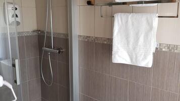 Une douche avec une porte en verre, un porte-serviettes avec une serviette et un distributeur de savon.