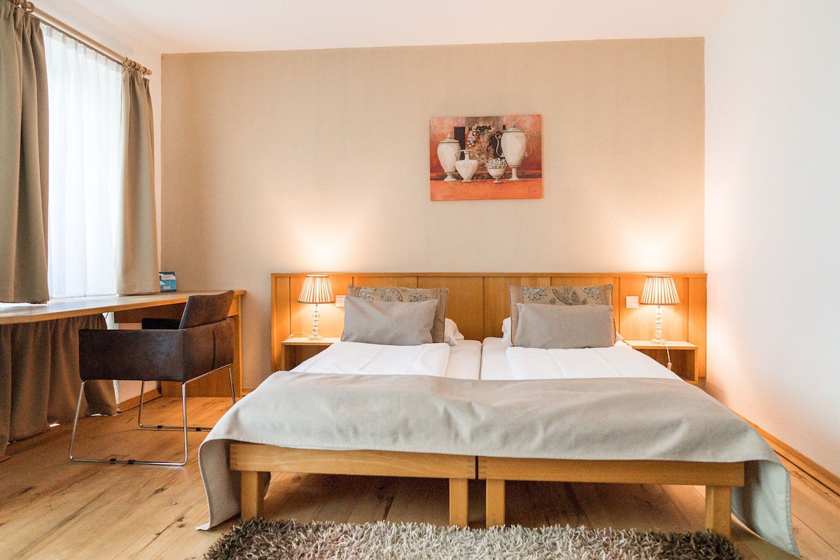 Camera d'albergo con un letto matrimoniale, due lampade sui comodini, una scrivania con sedia e un quadro appeso al muro.
