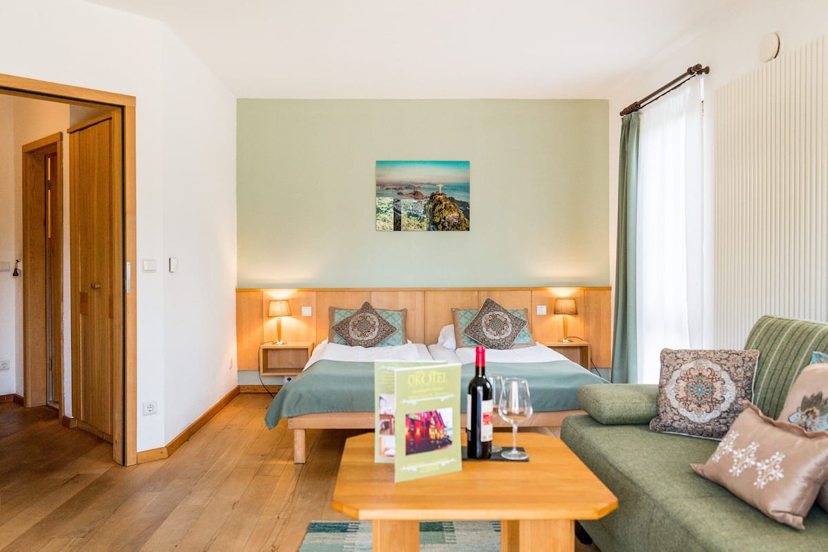 Una camera d'albergo con due letti, un divano verde, un tavolino in legno e un quadro appeso al muro.