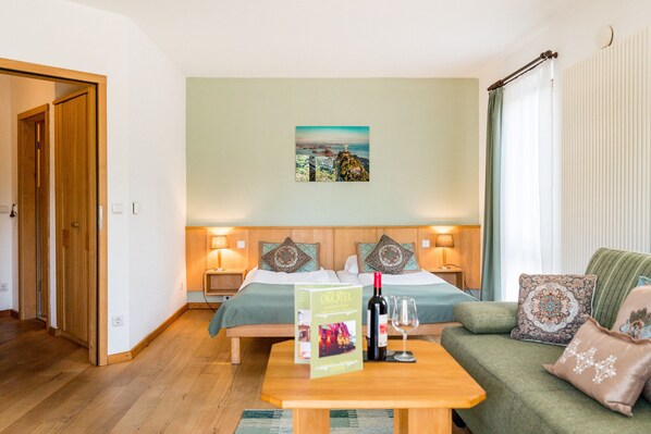 Habitación de hotel con dos camas, un sofá verde, una mesa de centro de madera y un cuadro en la pared.