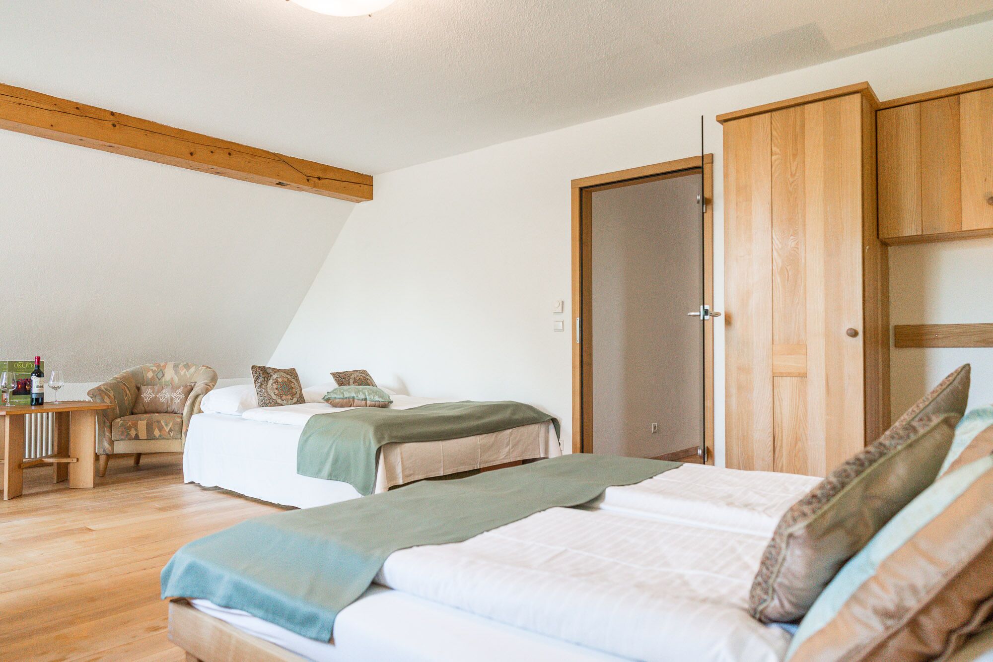 Une chambre avec deux lits, une armoire en bois, une petite table avec une chaise et une étagère fixée au mur.