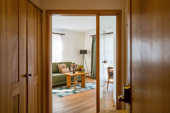 A wooden door leading into a living room with a green sofa, a small table with a lamp, and a chair.
