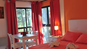 Habitación de hotel con cama, escritorio, silla, mesita de noche y ventana con cortinas.