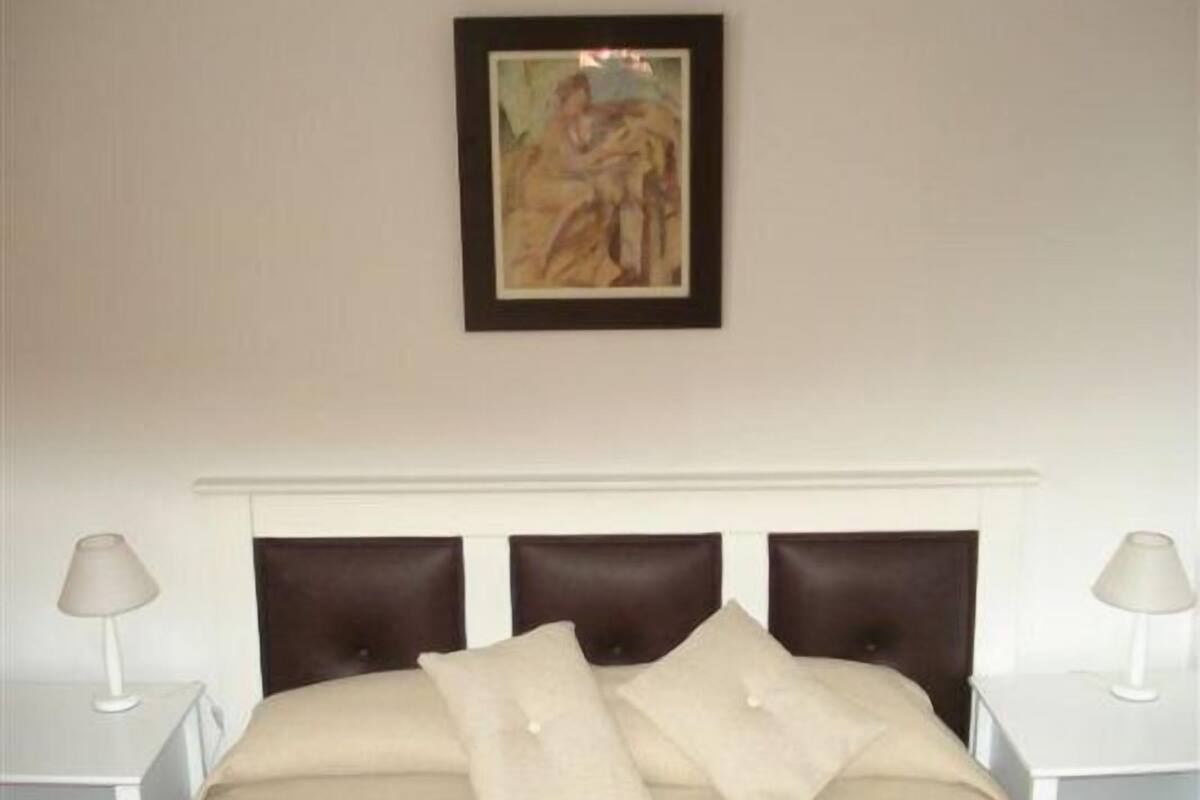 Un dormitorio con una cama, un cuadro enmarcado y dos lámparas de noche.