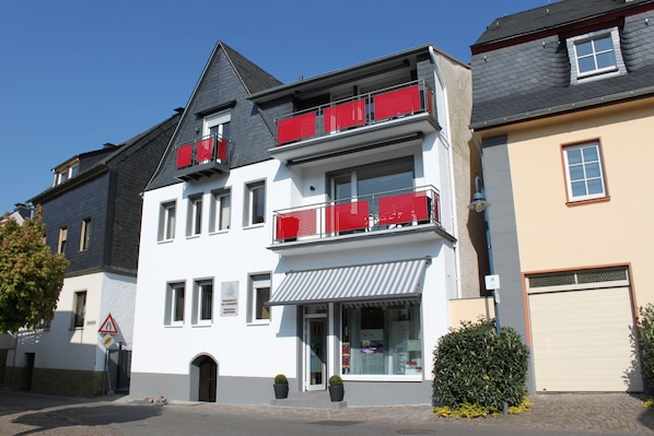 A two-story building with a white facade, red balconies, and a garage door.