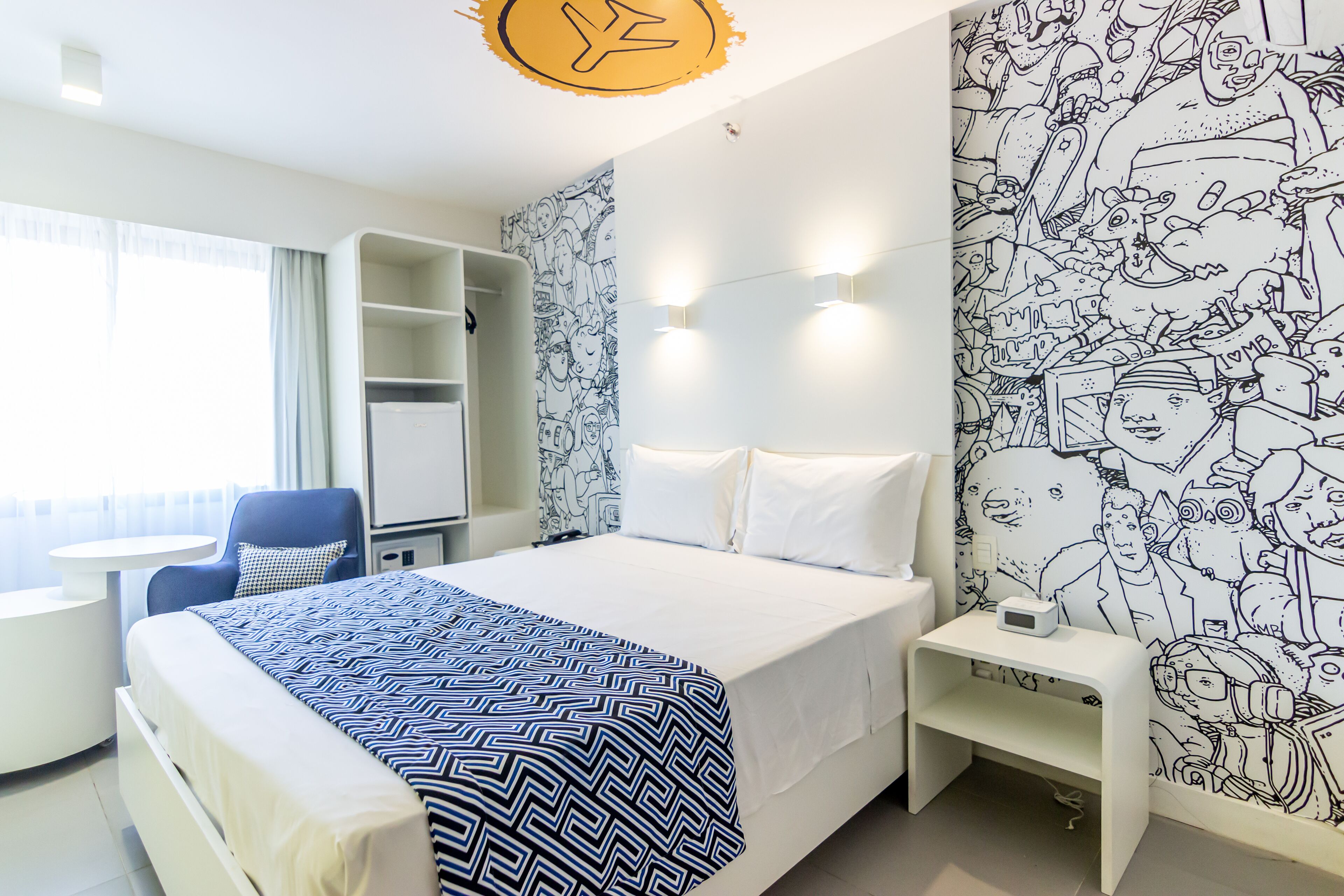 A hotel room with a bed, a desk, a chair, and a wall with a black and white mural.
