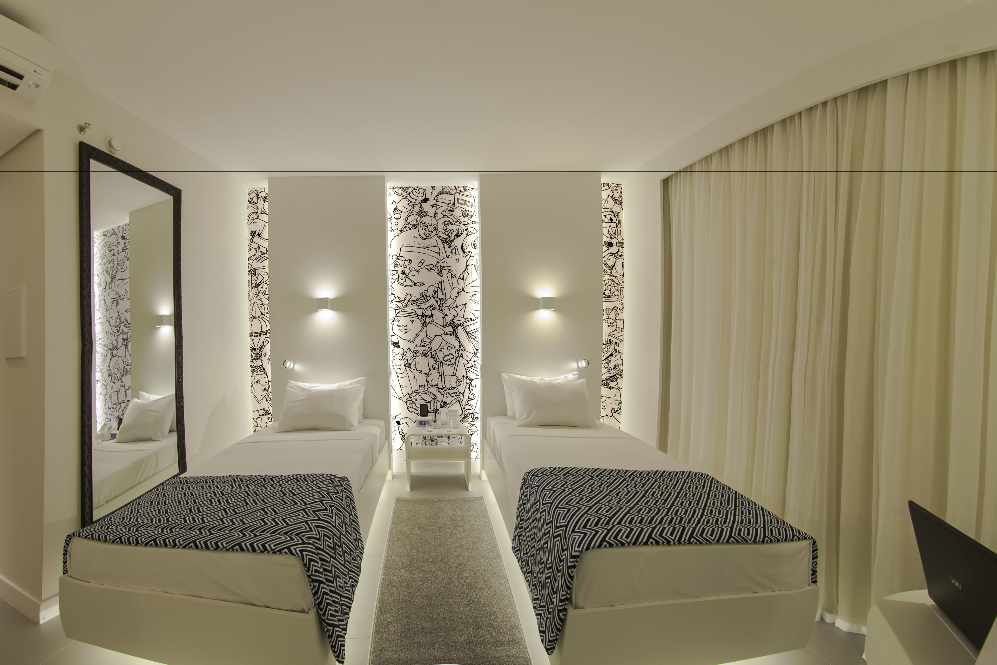 A hotel room with two beds, a central nightstand, a large mirror, and a curtain on the right.