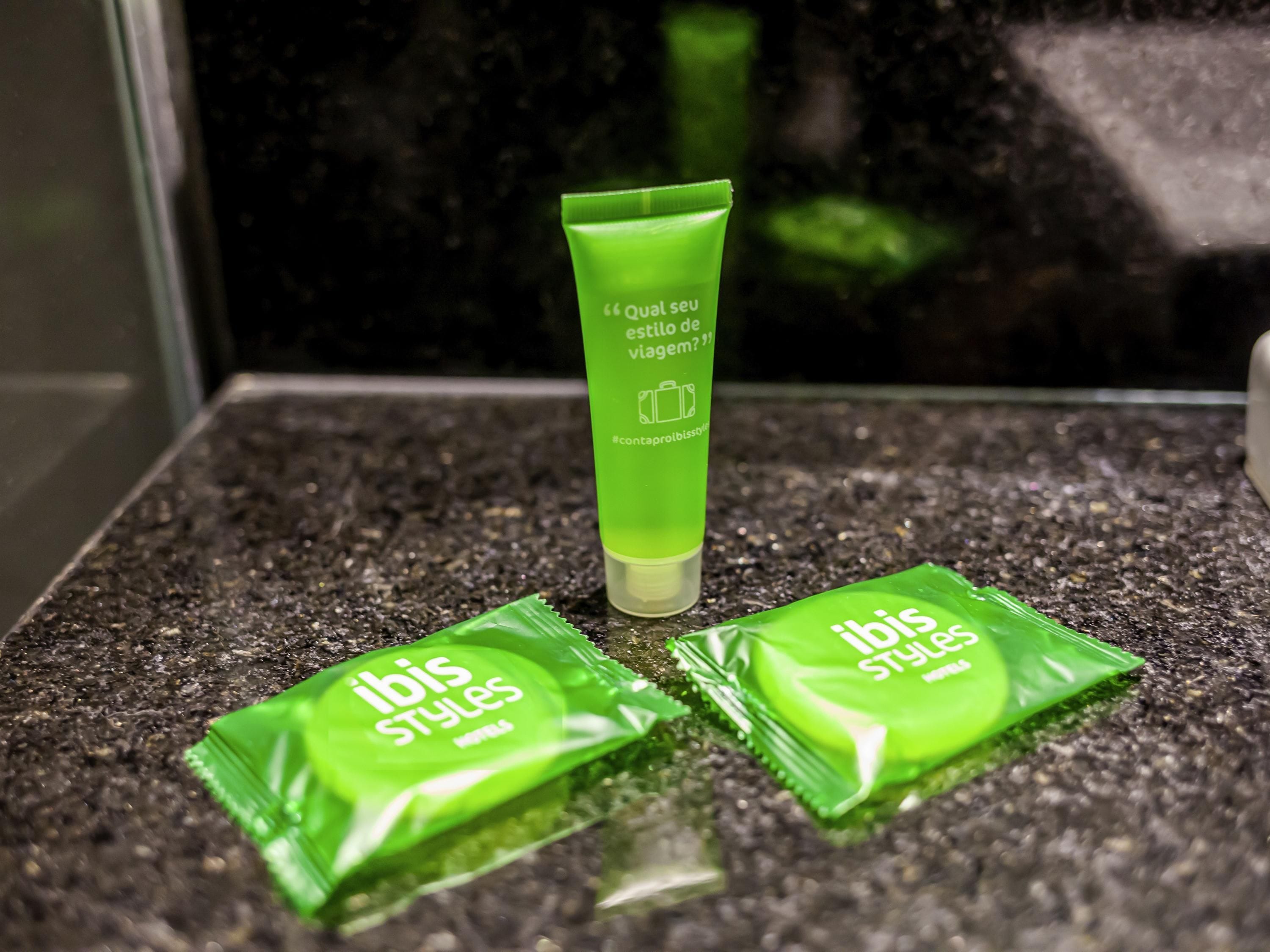 Un comptoir de salle de bain avec un tube vert et deux sachets verts portant la mention « Ibis Styles ».