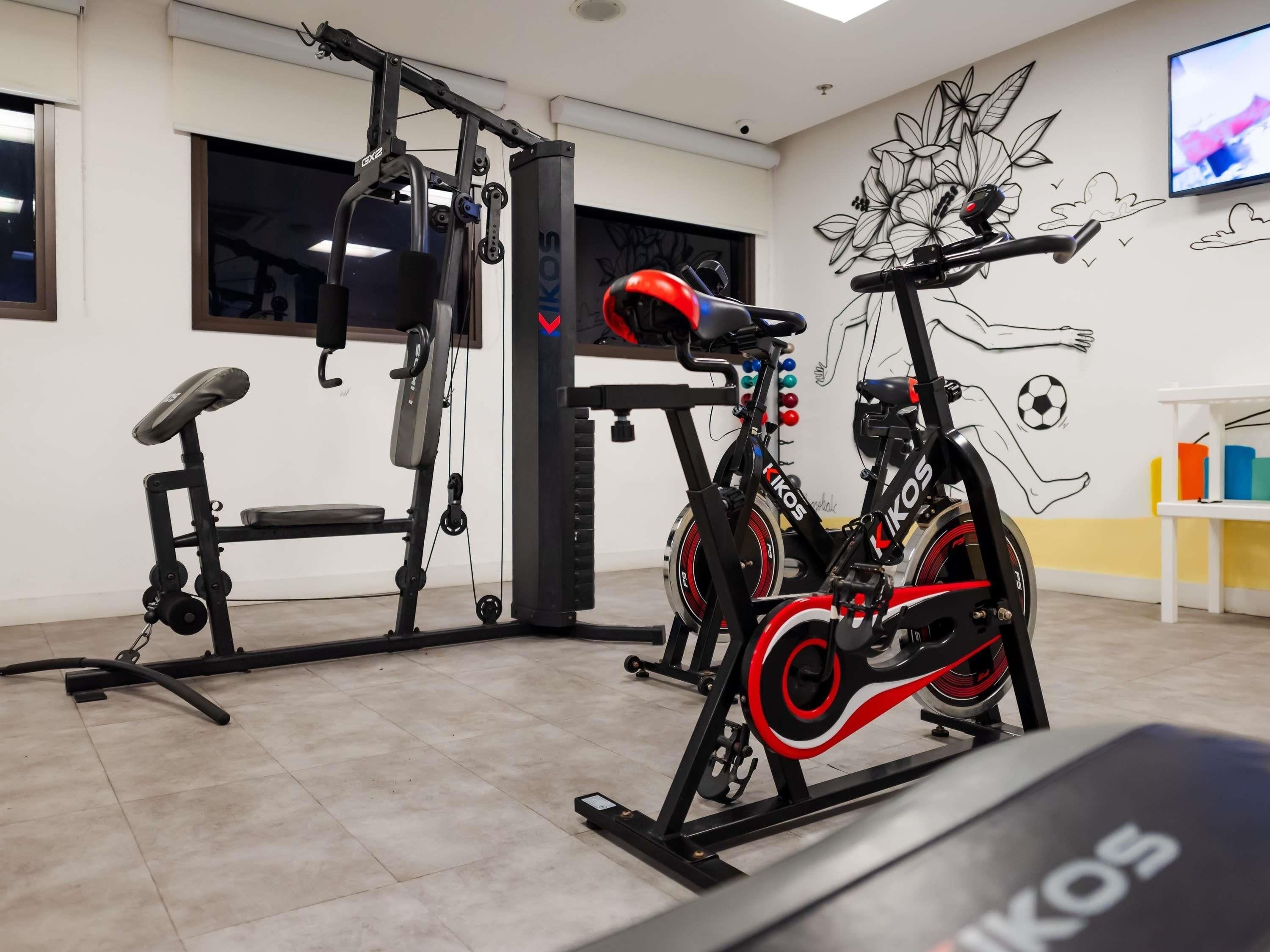 A gym with exercise equipment, a stationary bike, and a wall with sports illustrations.