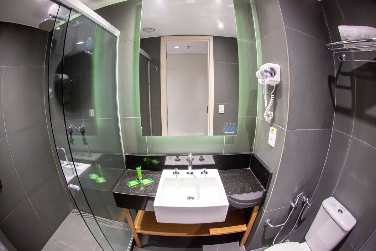 A modern bathroom with a glass-enclosed shower, a sink with a vanity, a toilet, and a hairdryer on a wall-mounted rack.