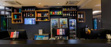 A hotel reception area with a counter, shelves with various items, a refrigerator, and a computer.