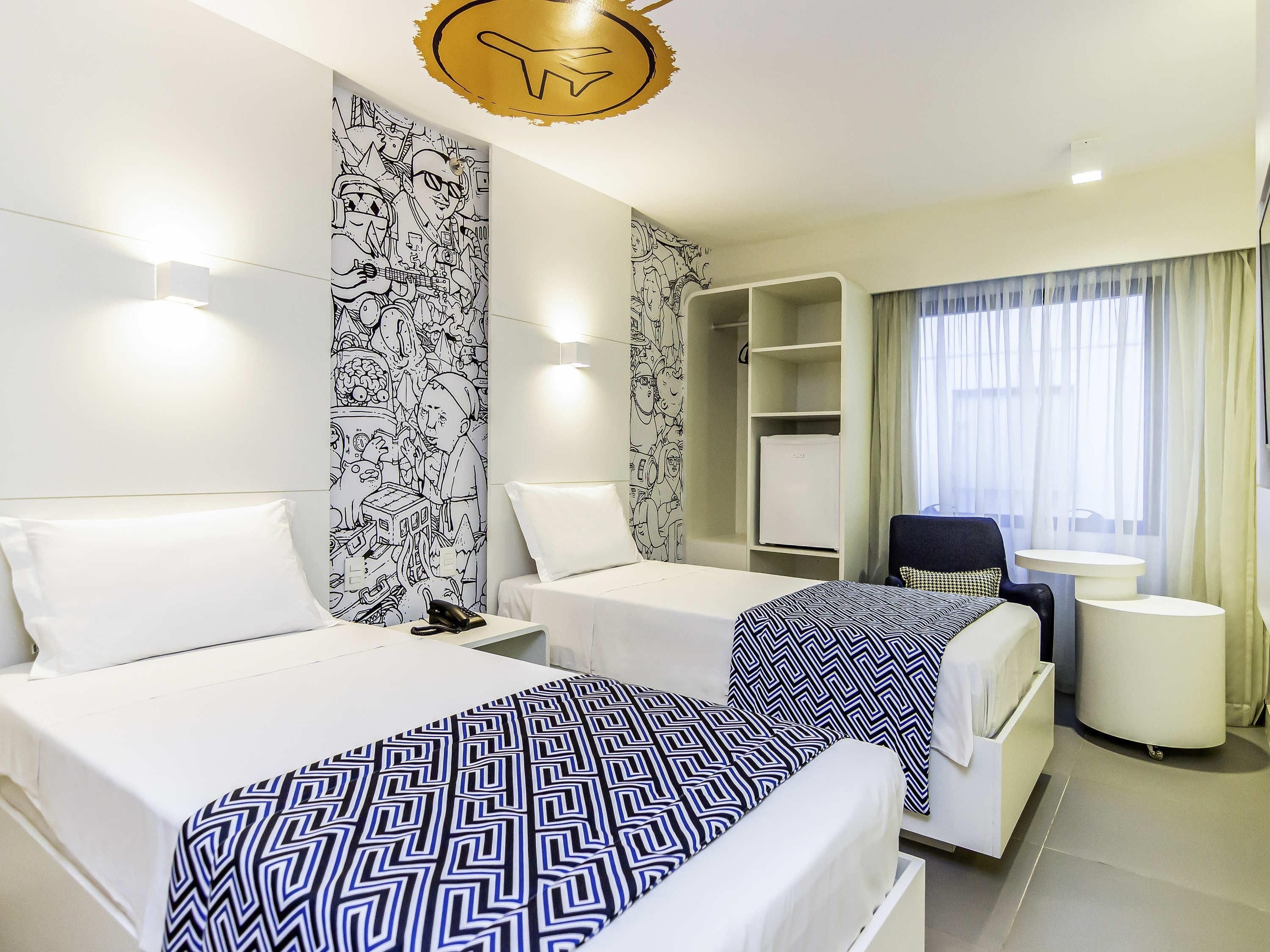 Habitación de hotel con dos camas, un escritorio, una silla, un armario y una ventana con cortinas.