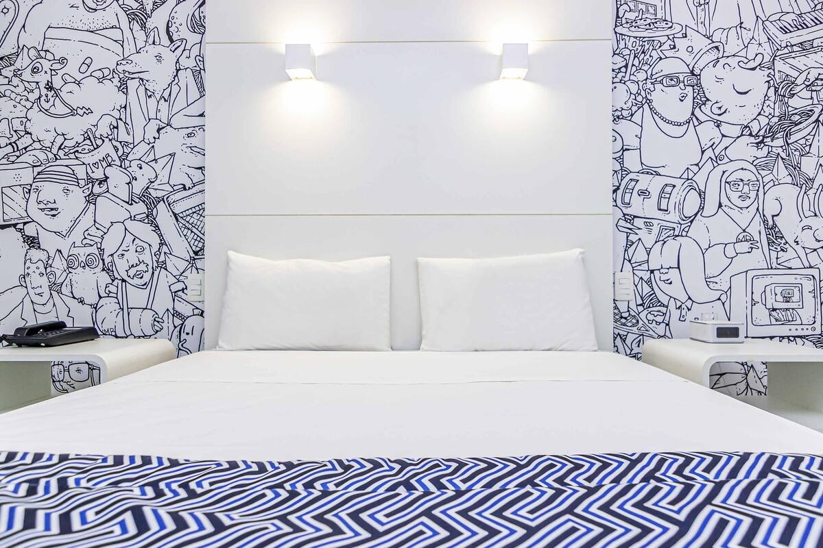 A bedroom with a bed, two bedside tables, a nightstand, and a wall with a black and white pattern.